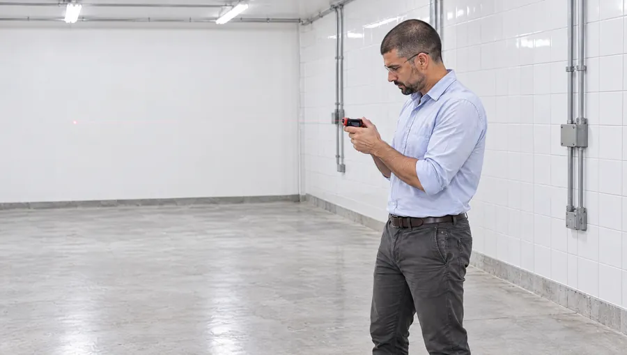 El Ingeniero de Estudio TREO mide con un medidor láser el depósito vacío de un supermercado donde van a ir las máquinas, mirando la pantalla del equipo